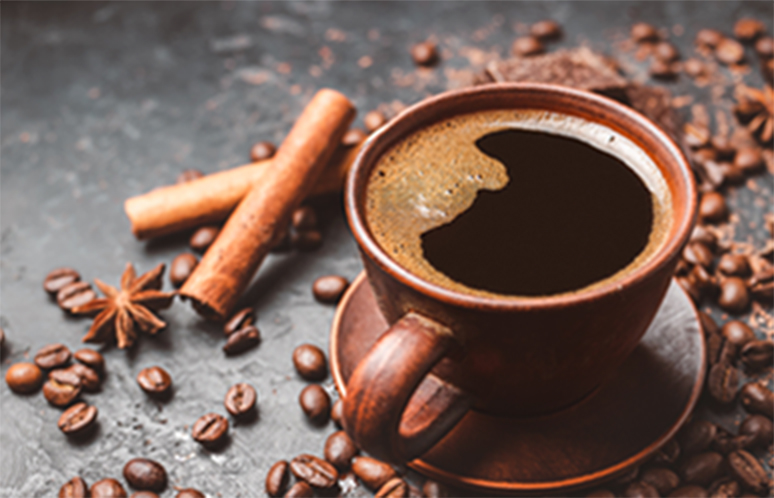 Fresh brewed black coffee in a cup on dark background with coffee beans and chocolate pieces.