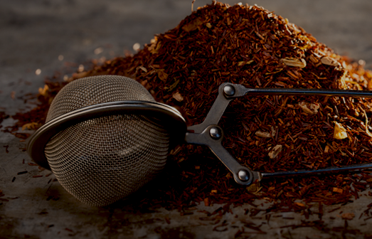 Dried Rooibos Tea and tea-strainer on a metal texture