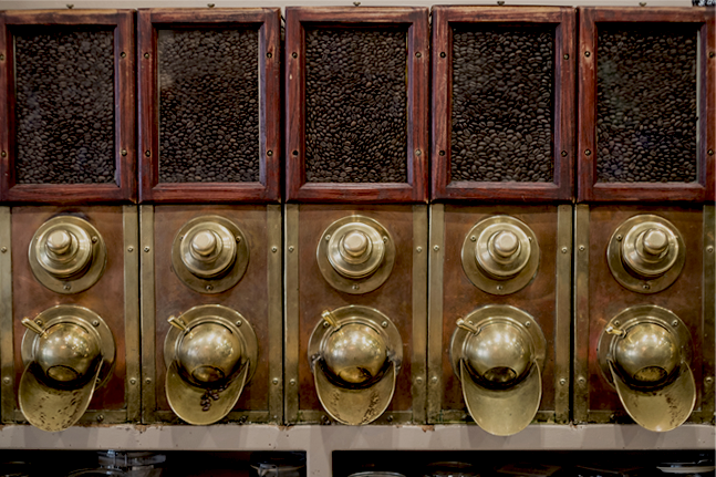 A variety of coffee beans in a wooden and brass dispenser