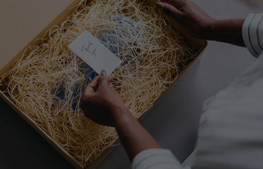 A woman unboxing a package with a thank you card inside. The box is filled with straw padding for protection.